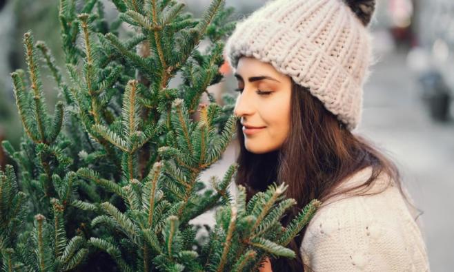 Frau mit heller gestrickter Mütze sieht sich Weihnachtsbäume an